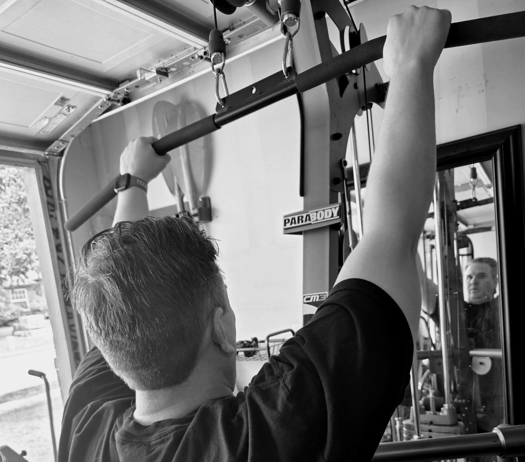 A client pulling down on a lat bar while his coach watches the lift in the mirror